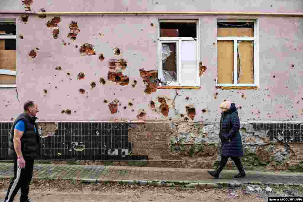 Плешан вітається із сусідкою, яка проходить повз один із ізюмських житлових будинків, понівечених війною. До вторгнення Росії в Ізюмі жили 45 000 людей. Після російської окупації, що тривала із квітня по вересень 2022 року, у місті залишилося менше 10 тисяч. Понад 80% житлового фонду зруйнована, як система водопостачання та опалення.