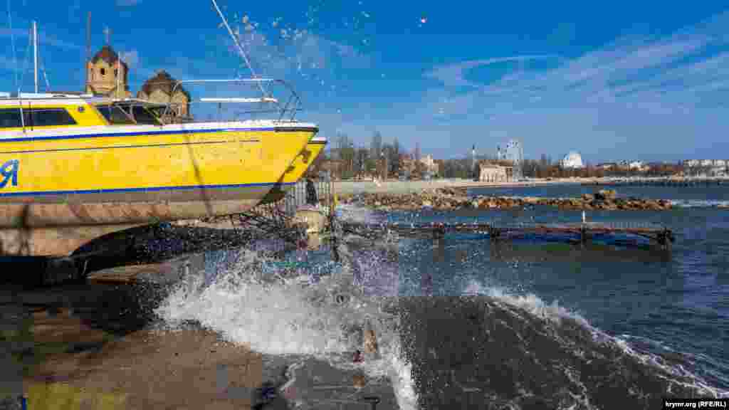 Бризки моря на причалі міського яхт-клубу. За яхтою видніються куполи Іллінської православної церкви Московського патріархату. А праворуч у небі &ndash; інверсійна &laquo;петля&raquo; від реактивного літака