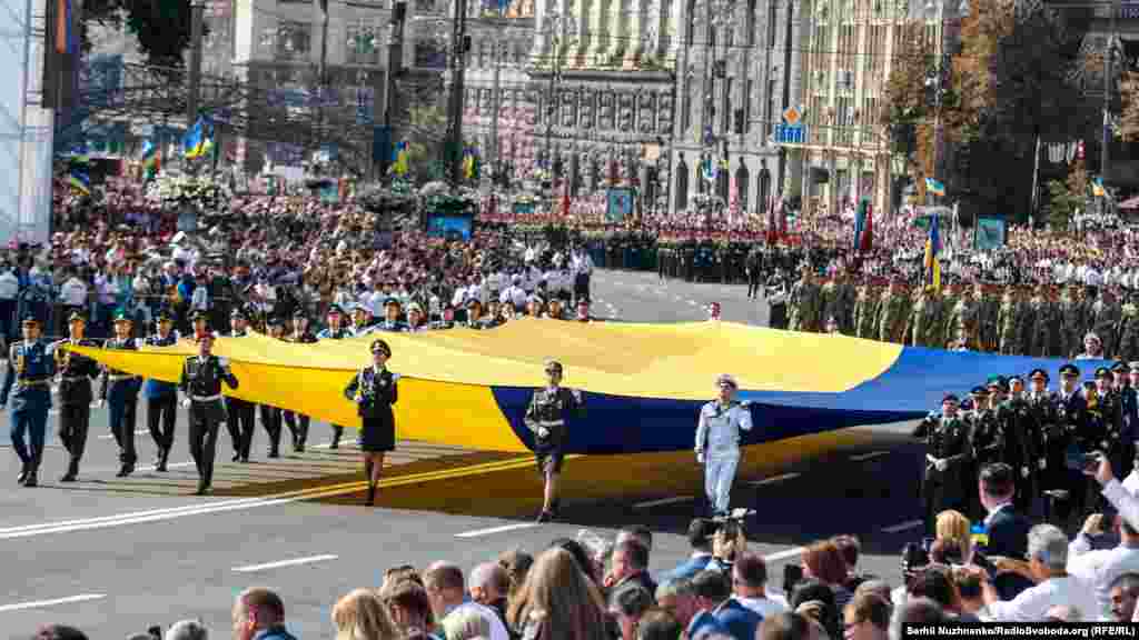 Центром столиці проносять великий Державний Прапор України. Стяг несе зведена група військових ЗСУ